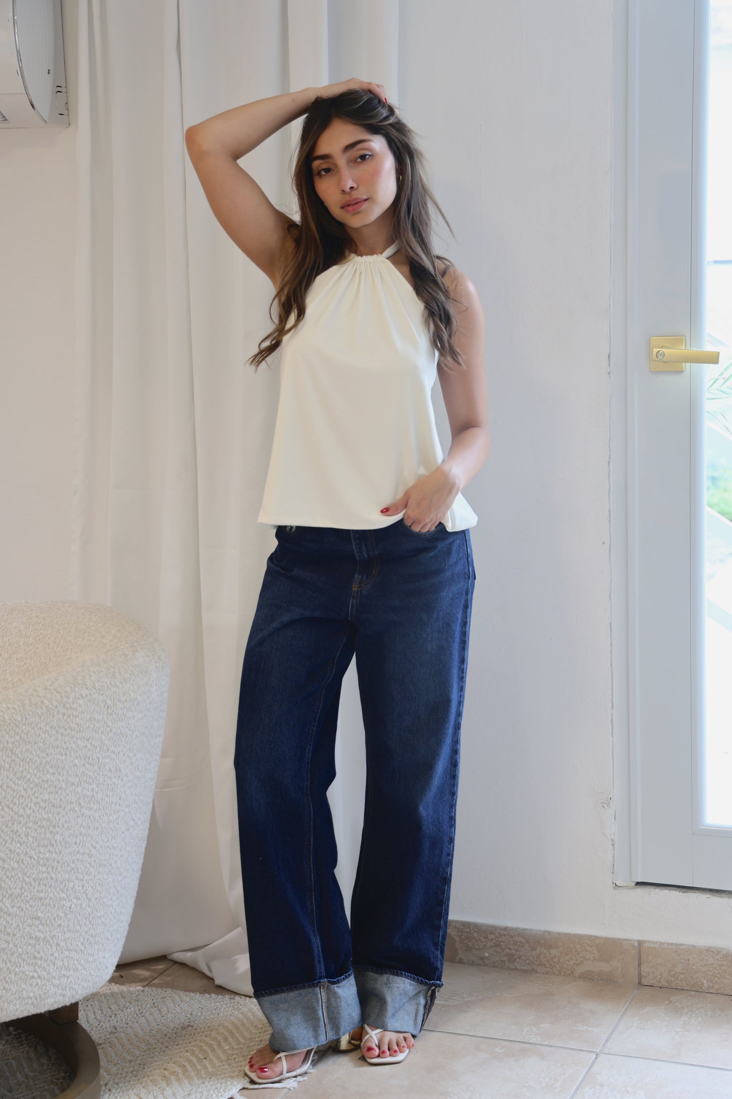 Woman wearing a white top and blue jeans standing indoors.