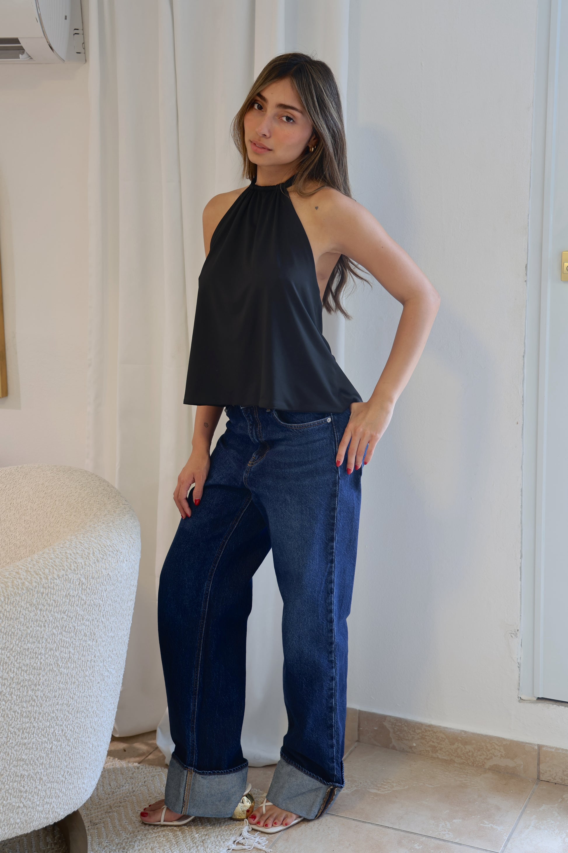 Woman wearing a black halter top and blue jeans indoors.