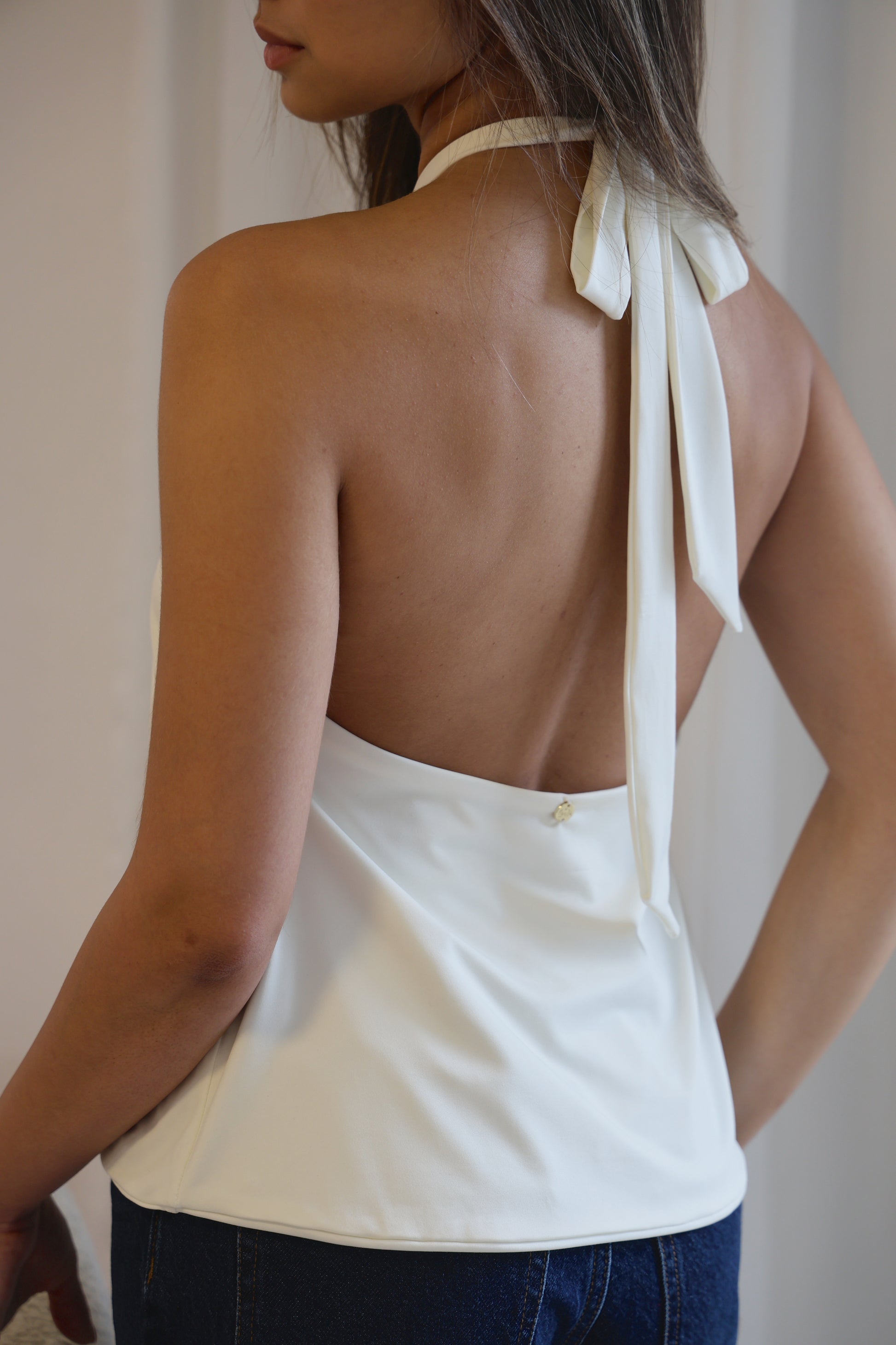 Woman wearing a white halter top with a bow detail on a plain background