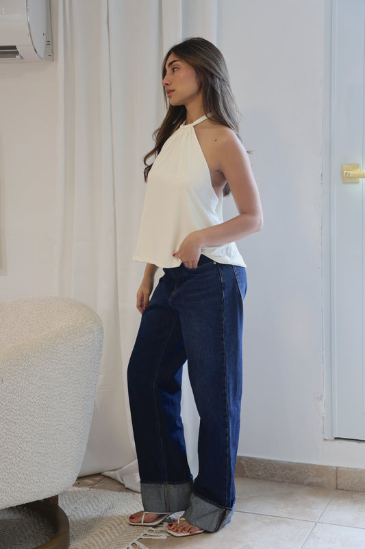 Woman wearing a white top and blue pants standing in a room with a white curtain and tiled floor.
