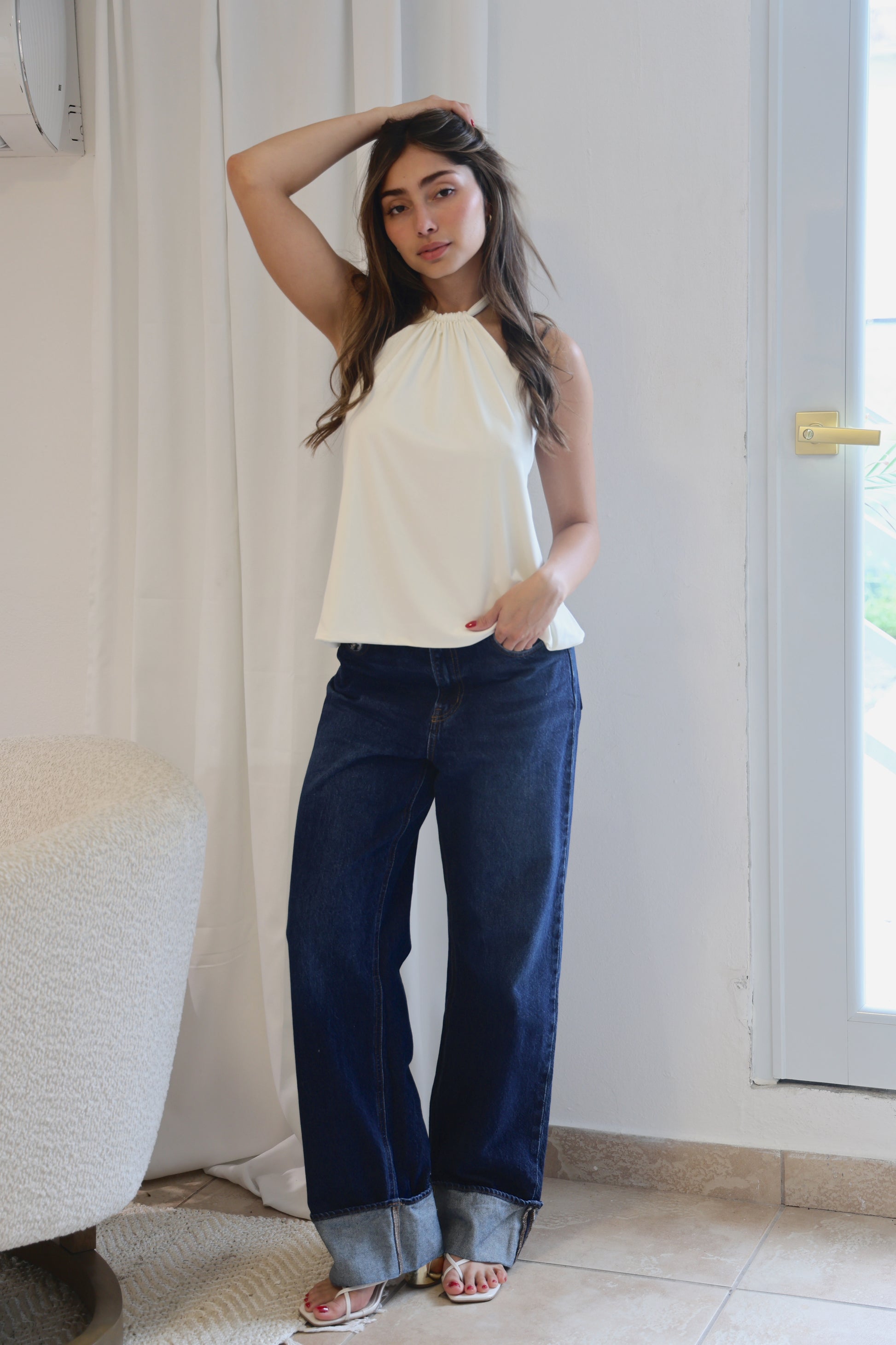 Woman wearing a white top and blue jeans standing indoors.